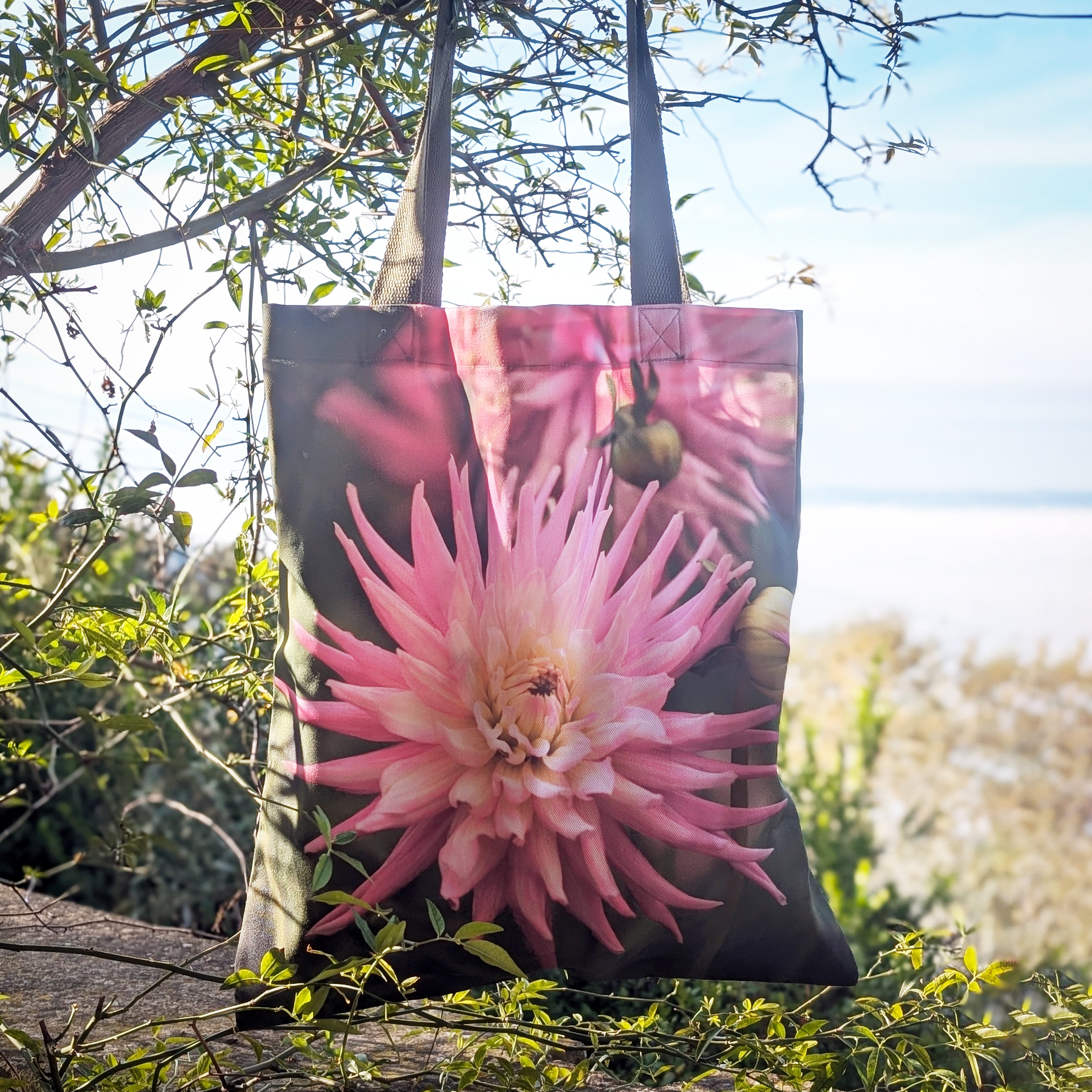 Tote bag with a pink flower design hanging among trees and plants.