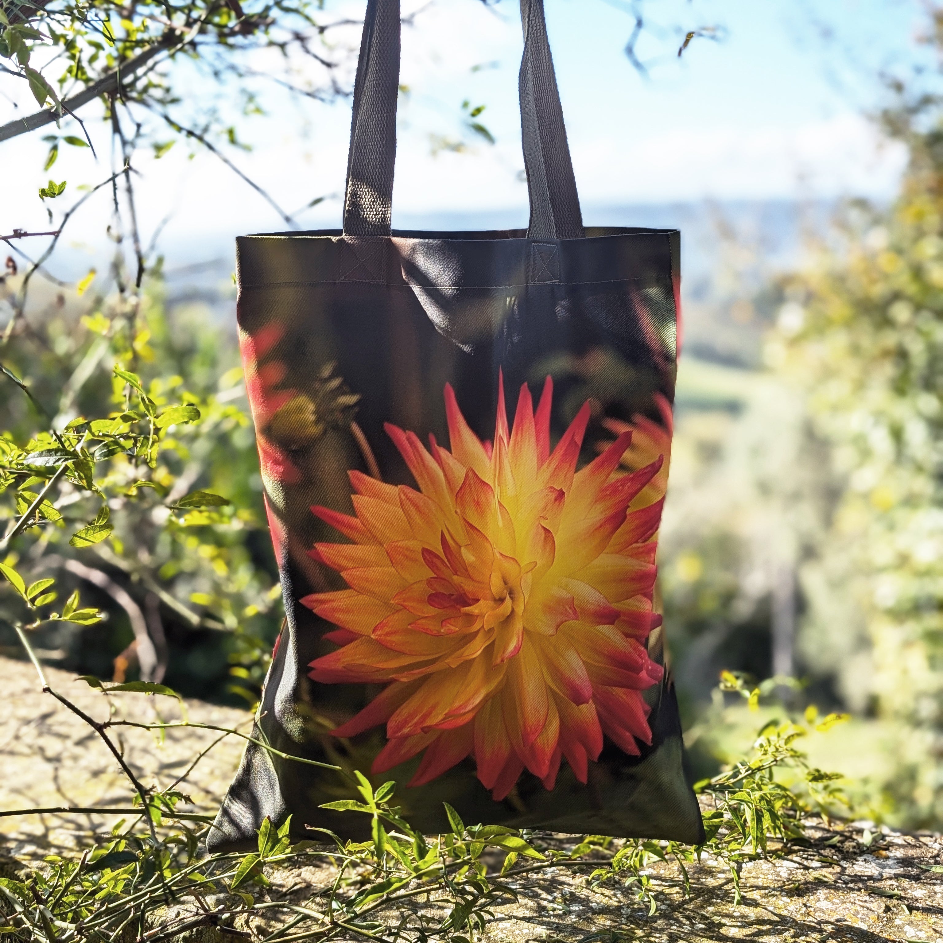 Tote bag with a large orange dahlia design in a natural setting